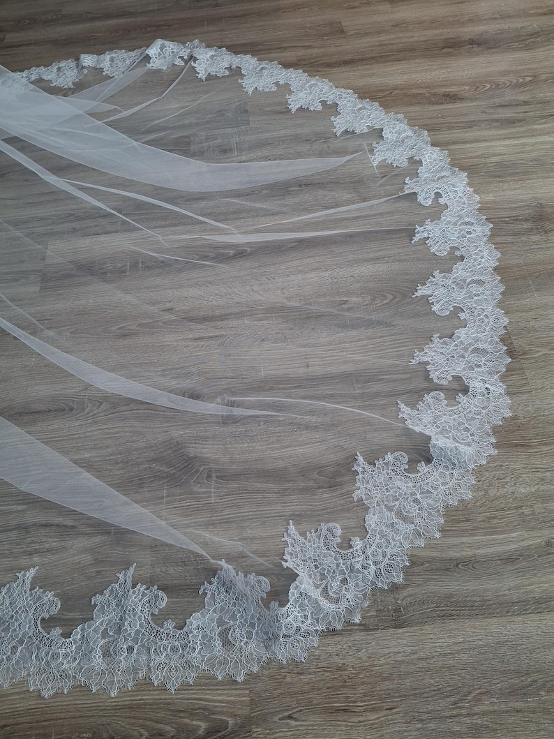 May include: A white bridal veil with a delicate lace trim. The lace is a floral pattern with a scalloped edge.