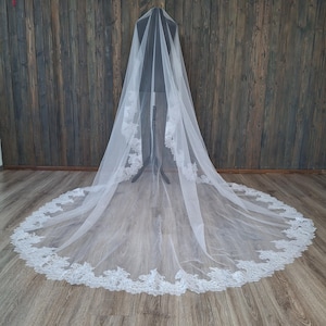 May include: A white bridal veil with a delicate lace trim. The veil is long and flowing, and it is displayed on a mannequin.