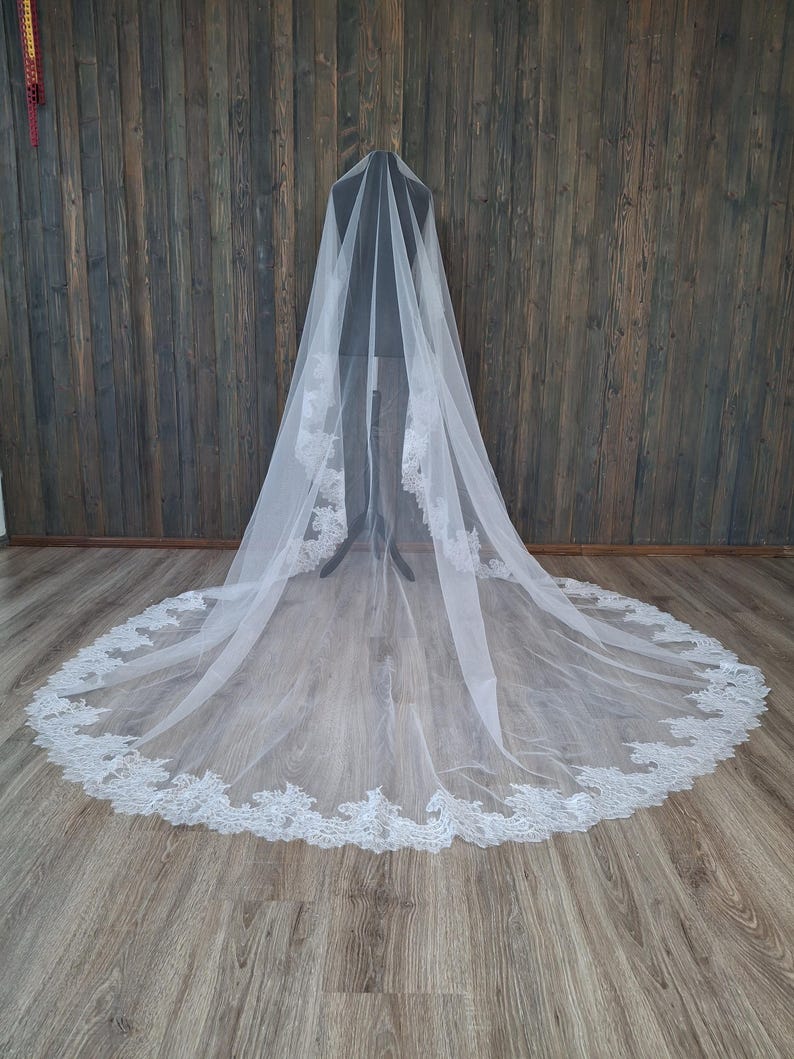 May include: A white bridal veil with a delicate lace trim. The veil is long and flowing, and it is displayed on a mannequin.