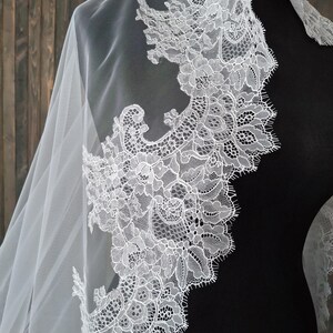May include: White bridal veil with a delicate lace trim. The lace features a floral pattern with intricate details.