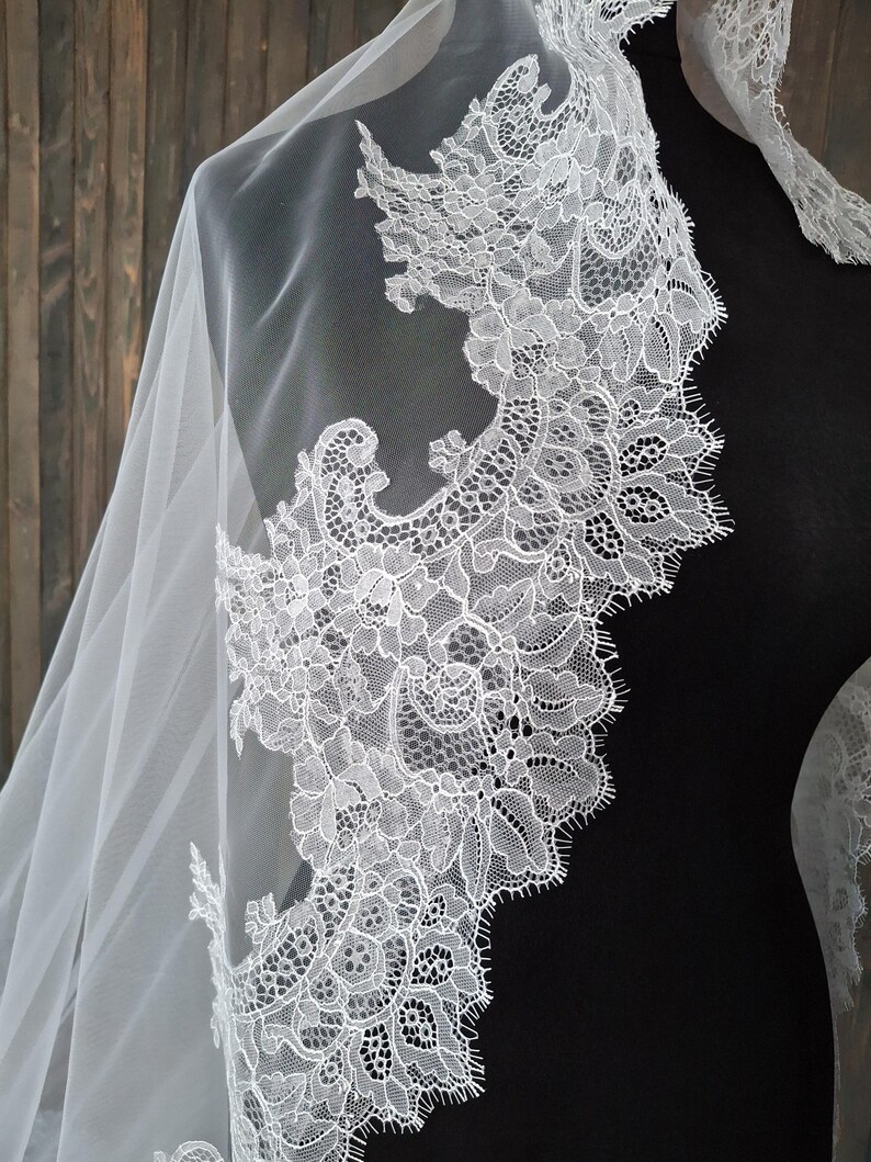 May include: White bridal veil with a delicate lace trim. The lace features a floral pattern with intricate details.