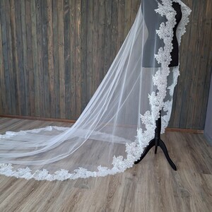 May include: A white bridal veil with a delicate lace trim. The veil is long and flowing, and it is draped over a mannequin.