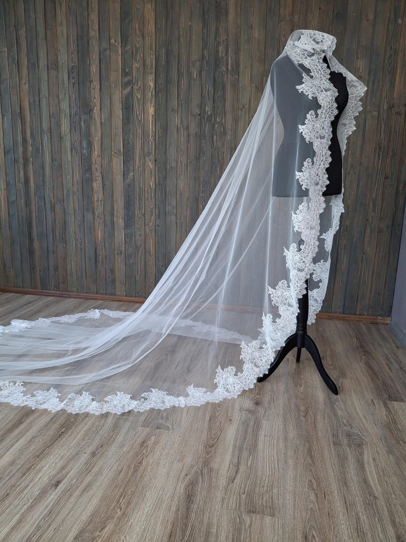 May include: A white bridal veil with a delicate lace trim. The veil is long and flowing, and it is draped over a mannequin.