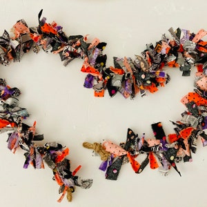 May include: A Halloween garland made of fabric scraps in black, orange, purple, and white with polka dots. The garland is in the shape of a heart.