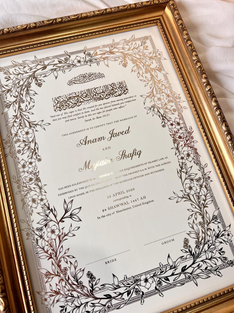 May include: A framed marriage certificate with gold accents and floral designs. The document features elegant calligraphy and the names Anam Javed and Mujtaba Shafiq. The frame is a gold color.