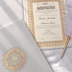 May include: A cream-coloured Islamic marriage certificate folder with gold foil calligraphy and intricate border patterns. The document inside lists the names Hussain Aboobaker and Sabreena Juma, dated July 2025, accompanied by a gold-toned feather pen.