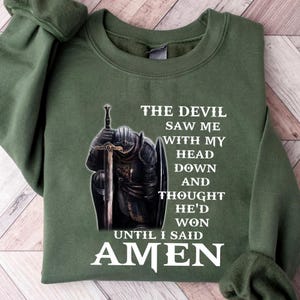 May include: Green sweatshirt with a white graphic of a knight kneeling with a sword. The text reads "The Devil Saw Me With My Head Down And Thought He'd Won Until I Said Amen."