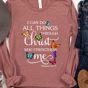 May include: A long-sleeved, mauve t-shirt with a white graphic design featuring butterflies and the text "I can do all things through Christ who strengthens me. Philippians 4:13".