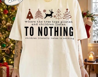 May include: An ivory t-shirt featuring a graphic of dark red Christmas trees, a reindeer, and snowflakes. The text reads: where the tree tops glisten and children listen TO NOTHING children literally listen to nothing.