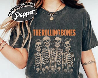 May include: Dark gray Comfort Colors t-shirt with the text "THE ROLLING BONES" in orange. The shirt features a graphic of four skeletons in a row. The word "Pepper" is in a white oval on the top left.