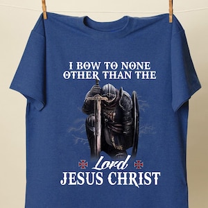 May include: A blue t-shirt with a white graphic of a knight kneeling with a sword and shield. The text on the shirt reads "I bow to none other than the Lord Jesus Christ".
