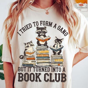 Może przedstawiać: Biały T-shirt z grafiką przedstawiającą trzy szopy czytające książki. Tekst na koszulce brzmi "Próbowałem stworzyć gang, ale zamienił się w klub książki".