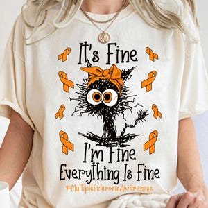 May include: A beige t-shirt featuring an orange ribbon design and a cartoon cat with the text "It's Fine I'm Fine Everything Is Fine #MultipleSclerosisAwareness"