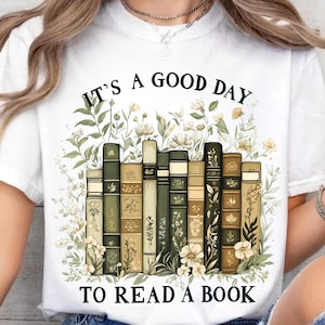 May include: White t-shirt with a green and brown illustration of a stack of books with flowers. The text "It's a good day to read a book" is printed on the shirt.