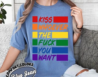 May include: A blue jean colored short-sleeve t-shirt featuring a graphic design with six horizontal colored bars in red, orange, yellow, green, blue, and purple. The text KISS WHOEVER THE FUCK YOU WANT is printed in white across the colored bars.