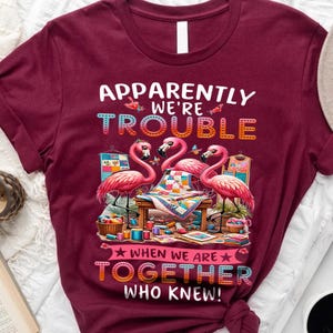 Może przedstawiać: Bordowy t-shirt z wzorem różowego flaminga i tekstem "Okazuje się, że jesteśmy kłopotem, kiedy jesteśmy razem, kto by pomyślał!"