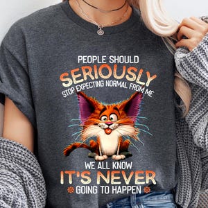 May include: Gray t-shirt with a cartoon cat and the text "People should seriously stop expecting normal from me. We all know it's never going to happen."