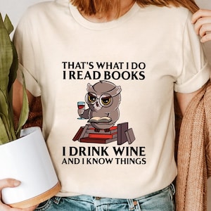 Puede incluir: Una camiseta blanca con un gráfico de un búho leyendo un libro y sosteniendo una copa de vino. El texto en la camiseta dice "That's what I do I read books I drink wine and I know things."