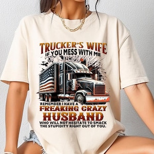 Puede incluir: Camiseta beige con un gráfico de un camión y el texto: "Trucker's Wife, If You Mess With Me, Remember I Have A Freaking Crazy Husband Who Will Not Hesitate To Smack The Stupidity Right Out Of You."