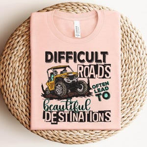 May include: Pink t-shirt with a graphic of a yellow off-road vehicle and the text "Difficult roads often lead to beautiful destinations."