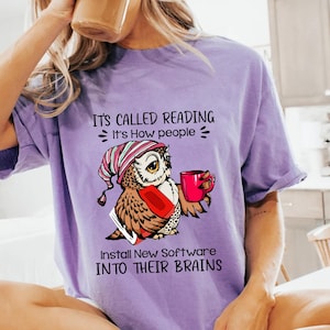 May include: Purple t-shirt with a graphic of an owl wearing a hat and holding a cup of coffee. The text on the shirt reads "It's called reading. It's how people install new software into their brains."