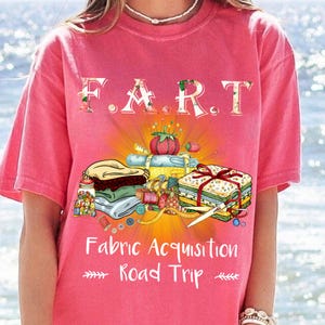 May include: Pink t-shirt featuring the text "F.A.R.T. Fabric Acquisition Road Trip" and an illustration of sewing supplies, including fabric, buttons, and a measuring tape.