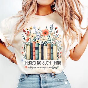 May include: A white t-shirt featuring a graphic of a stack of books surrounded by colourful flowers. The text "THERE'S NO SUCH THING as too many books" is printed below the graphic.