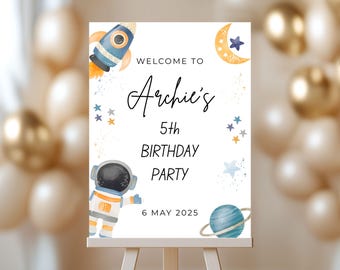 May include: A white sign on an easel with the text "Welcome to Archie's 5th Birthday Party 6 May 2025." The sign features illustrations of a rocket ship, astronaut, moon, stars, and a planet with rings. The background includes balloons.