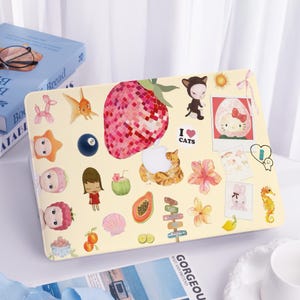 May include: A light yellow laptop case decorated with various stickers. The stickers feature a large strawberry, a cat, a Hello Kitty image, and the words "I ❤️ CATS". Other stickers include a seahorse, a bunny, and a goldfish.