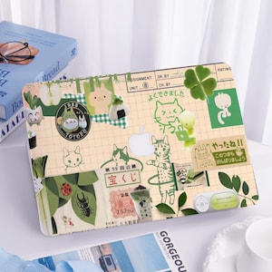 Könnte beinhalten: Ein Laptop mit einem grünen und weißen Sticker-Design. Die Sticker zeigen verschiedene Bilder, darunter Katzen, Pflanzen und japanische Schriftzeichen. Der Text auf den Stickern lautet "1988", "Totoro", "よくできました", "宝くじ", "やったね!!", und "このつぎもがんばりましょう".