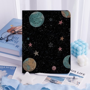 May include: Black tablet case with a space-themed design, including planets, stars, and a comet. The case has a dark background with colourful illustrations. A white stylus is placed in front of the case.