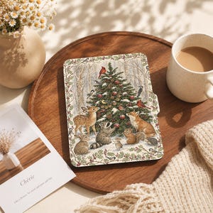 May include: A rectangular e-reader skin featuring a detailed illustration of a snow-covered Christmas tree in a forest. The scene includes a deer, a raccoon, a fox, a squirrel, a hedgehog, and various birds, all framed by a holly berry border.