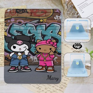 Könnte beinhalten: Eine Tablet-Hülle mit einer Cartoon-Illustration von zwei Figuren vor einer Graffiti-Wand. Eine ist schwarz mit einem Totenkopf, die andere ist Hello Kitty. Beide tragen goldene Ketten und zeigen den Mittelfinger. Der Name "Mary" steht unten.
