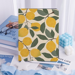 May include: A tablet case featuring a lemon and leaf pattern on a cream background. The design includes yellow lemons and green leaves on brown branches. A white stylus rests on the surface.