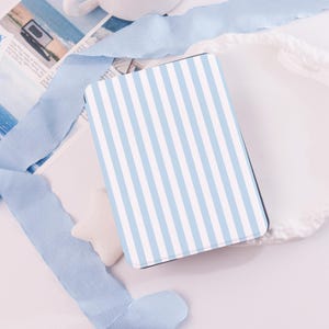 Könnte beinhalten: Eine rechteckige Hülle mit blau-weißem Streifenmuster. Umgeben von hellblauem Band, einem weißen sternförmigen Objekt und einer weißen Oberfläche. Wahrscheinlich eine Hülle für ein Tablet oder einen E-Reader.