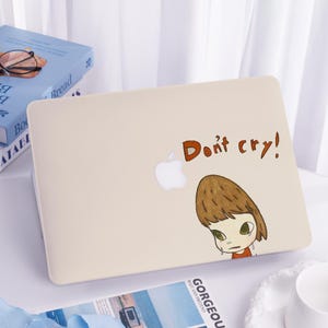 May include: A beige laptop case with the text "Don't cry!" in brown letters. The case features a white Apple logo and a cartoon illustration of a crying girl with brown hair and green eyes.