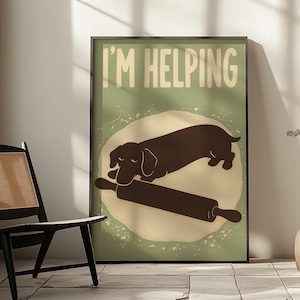 Peut inclure: Une affiche murale rectangulaire dans un cadre noir représentant la silhouette d'un teckel brun foncé posé sur un rouleau à pâtisserie sur une forme de pâte beige contre un fond vert sauge avec le texte I'M HELPING en lettres blanches.