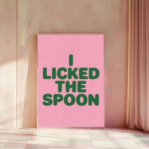 Peut inclure: Une affiche murale rectangulaire présentant un fond rose clair uni avec le texte vert foncé I LICKED THE SPOON écrit dans une police sans empattement grasse et arrondie. L'impression est encadrée par un fin cadre doré.