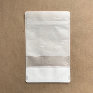 May include: A white stand-up pouch with a clear window. The pouch has a zipper closure and is made of a durable material.