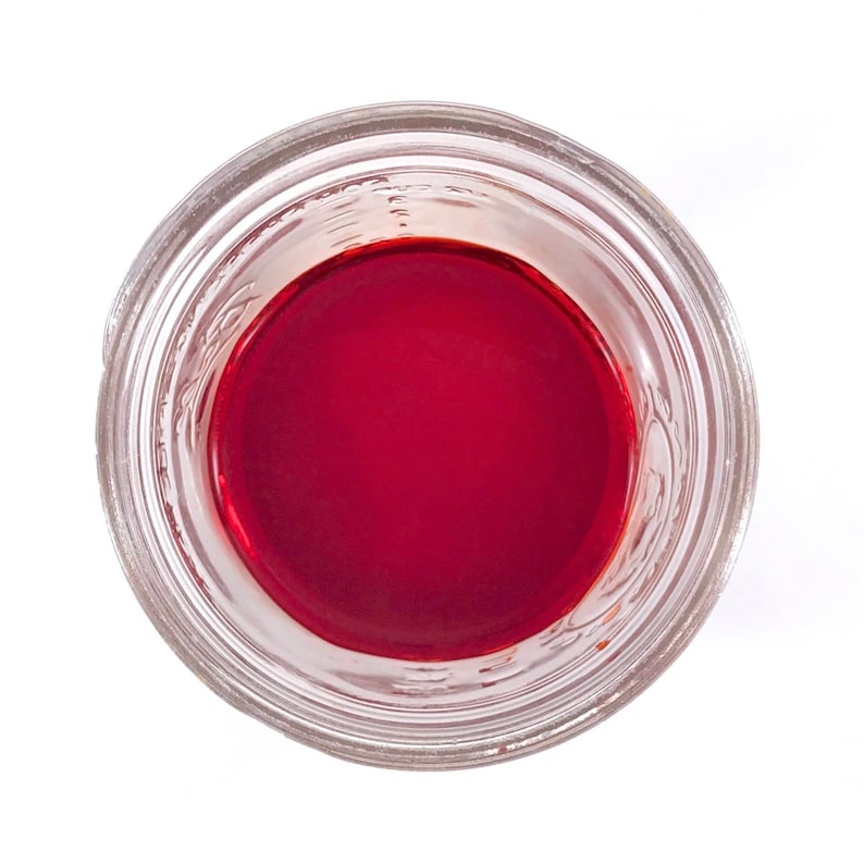 May include: A clear glass jar with a red liquid inside. The jar has a wide mouth and a smooth rim.