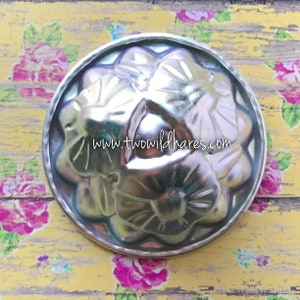 Peut inclure: Un moule en métal argenté pour cuire un gâteau ou un dessert. Le moule a un motif floral avec trois grandes fleurs. Le moule est sur un fond floral jaune et blanc.