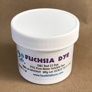 Może przedstawiać: Biały plastikowy słoik z białą pokrywką zawierający barwnik fuksjowy. Etykieta zawiera napis "FUCHSIA DYE", "D&C Red 33 Dye", "95% Pure Water Soluble Dye", "FDA Lot #AY4969", "Mfg Lot: DCR33-1617/118" oraz "www.TwoWildHares.com".