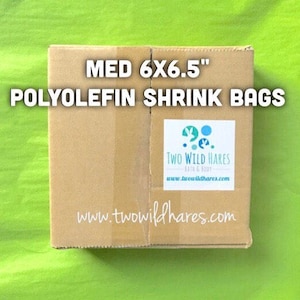 May include: A brown cardboard box with the text "MED 6X6.5" POLYOLEFIN SHRINK BAGS" printed on the front. A white label with the text "TWO WILD HARES BATH & BODY www.twowildhares.com" is on the right side of the box. The text "www.twowildhares.com" is printed on the bottom of the box.