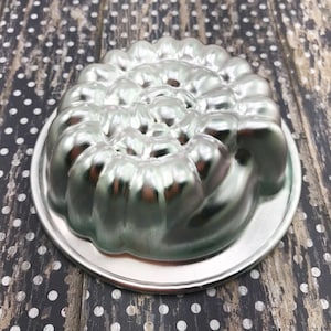 May include: A silver metal mold shaped like a spiral, with a smooth, shiny surface. The mold is designed for baking cakes or other desserts.