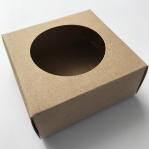 Puede incluir: Una caja de cart&oacute;n marr&oacute;n con un recorte circular en la parte superior. La caja est&aacute; vac&iacute;a.