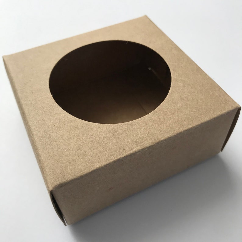 Puede incluir: Una caja de cart&oacute;n marr&oacute;n con un recorte circular en la parte superior. La caja est&aacute; vac&iacute;a.