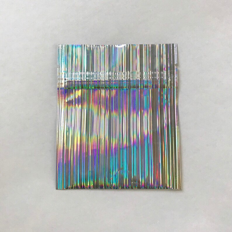 May include: A silver iridescent plastic bag with a heat-sealed opening. The bag is made of thin, flexible plastic and has a holographic finish.