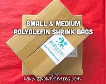 Puede incluir: Dos cajas de cartón apiladas una encima de la otra. La caja superior tiene una etiqueta que dice "Two Wild Hares Bath & Body" y "www.twowildhares.com". La caja inferior tiene el texto "www.twowildhares.com" impreso en ella. Las cajas están sobre una superficie roja. El texto "SMALL & MEDIUM POLYOLEFIN SHRINK BAGS" está impreso en las cajas.