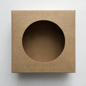 Puede incluir: Una caja de cart&oacute;n marr&oacute;n con un recorte circular en el centro. La caja est&aacute; dise&ntilde;ada para el embalaje y el env&iacute;o.