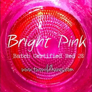 May include: Close-up of a bright pink circle with concentric rings. The text "Bright Pink" is written in white across the center of the circle. Below the text is "Batch Certified Red 28" and the website "www.twowildhares.com".
